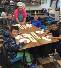 Students participate in a food activity with a staff member in a chef hat