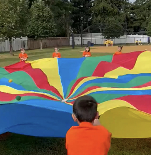 Teacher and students holding open a colorful parachute