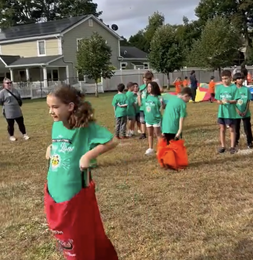 Students in green t-shirts jumping in potato sacks